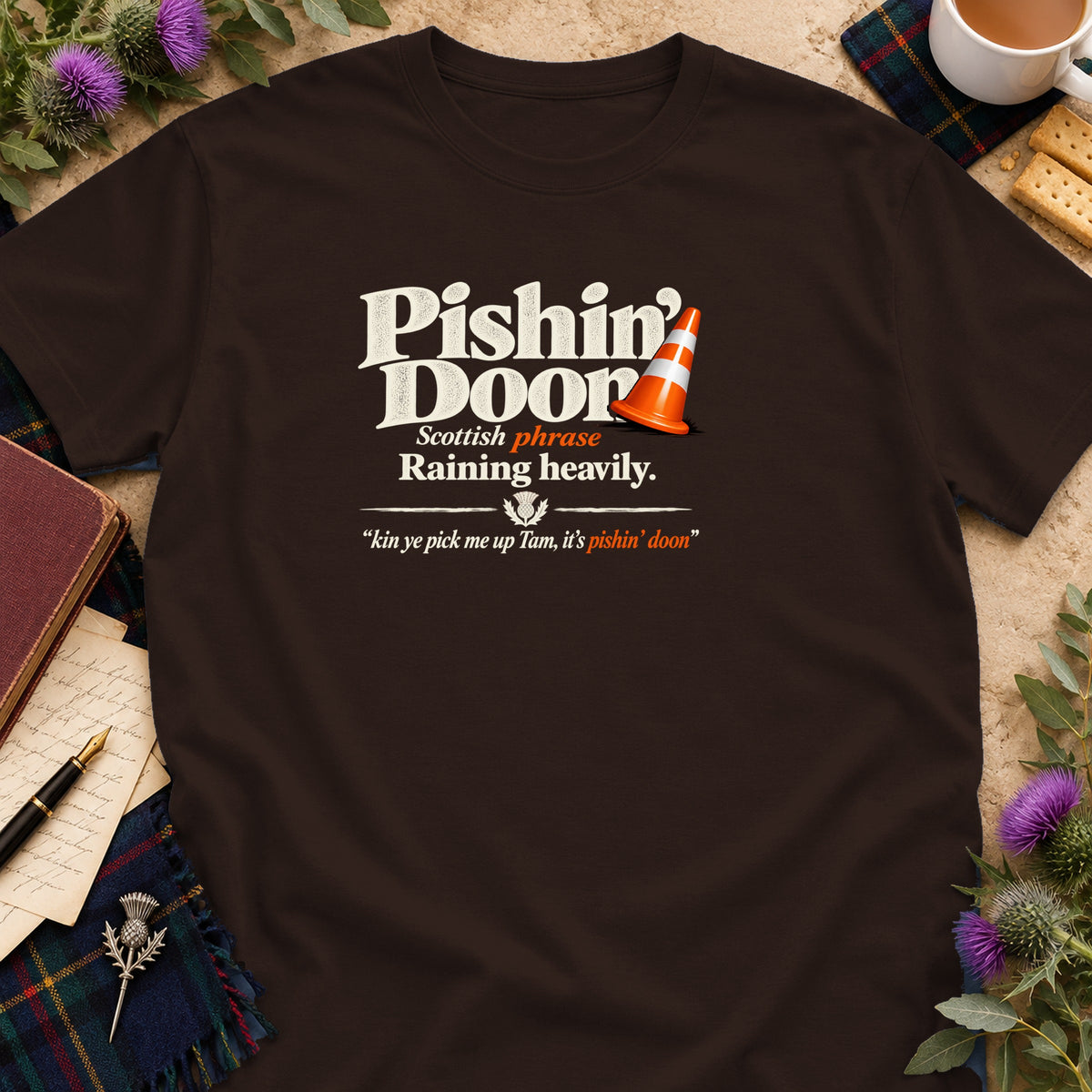 Brown t-shirt featuring distressed white and orange text that reads Pishin Doon Scottish phrase Raining heavily.