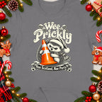 Hedgehog wearing a Santa hat holding an orange cone with text "Wee Prickly Nae Scotland, Nae Party".