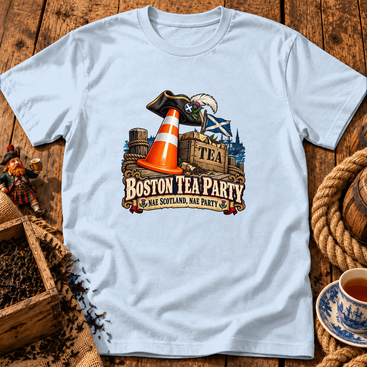 A light blue t-shirt with a graphic of a pirate hat, traffic cone, and tea crate, featuring the text "Boston Tea Party, Nae Scotland, Nae Party".