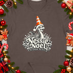 Nessie Noel graphic with "Nae Scotland, Nae Party." text on a brown t-shirt.